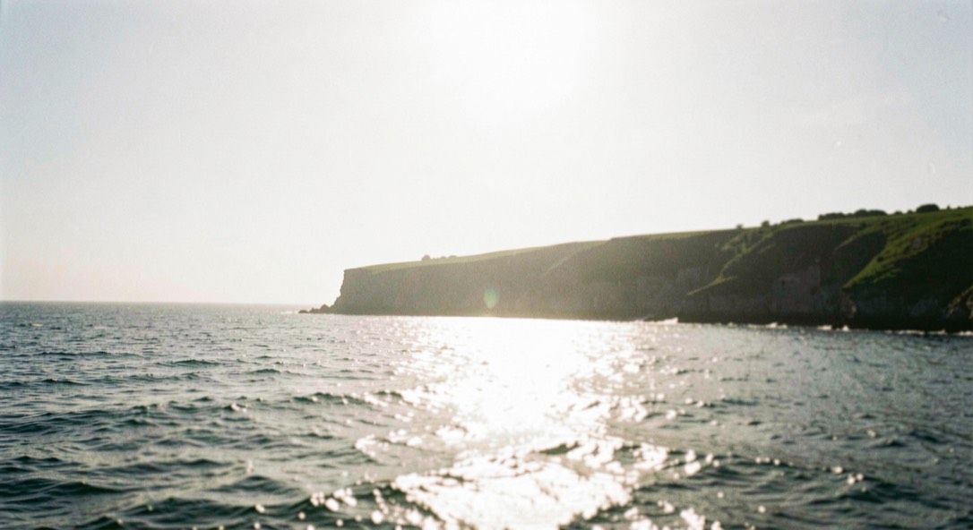Bright hazy sea under a high sun with strong glare and a low green headland in shadow